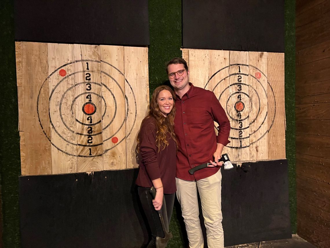 A lab member and his wife smile while standing in front of the axe throwing bullseye