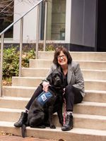 Paula Crawford-Gamble posing on the steps with service dog Dollie, a black lab