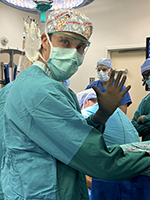 Chris Naimo in the operating room wearing scrubs, a mask, and gloves