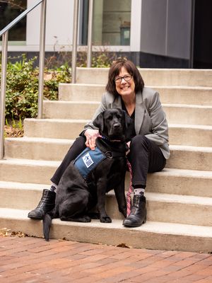 Paula Crawford Gamble posing with service dog Dollie, a black lab