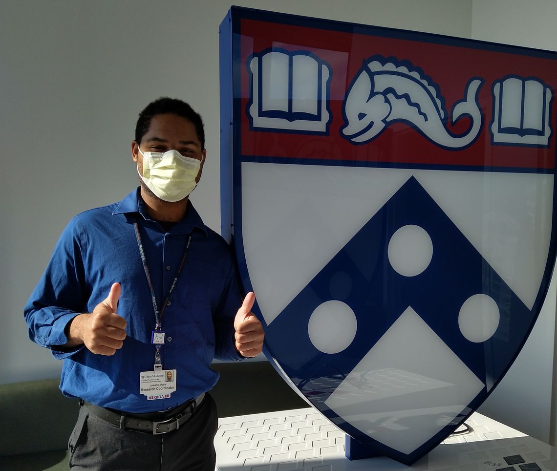 CCRU coordinator Juwann Moss standing next to a large Penn Logo sign giving two thumbs up.