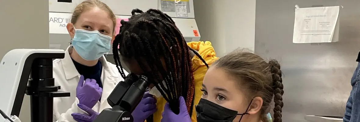 Three students in a laboratory with one student looking through a microscope