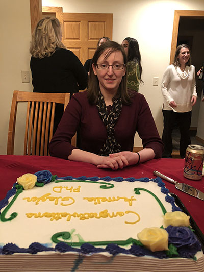 A woman who just received her PhD sitting in front of a celebration cake. 