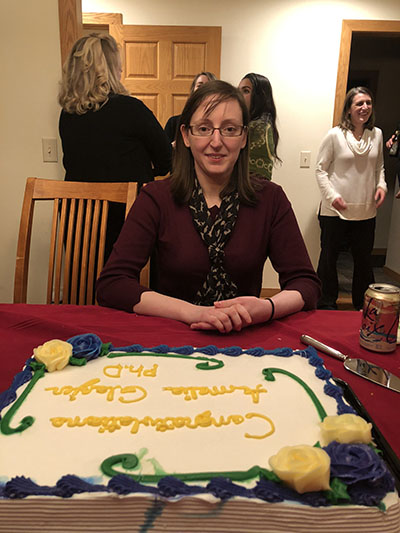 A woman who just received her PhD sitting in front of a celebration cake.