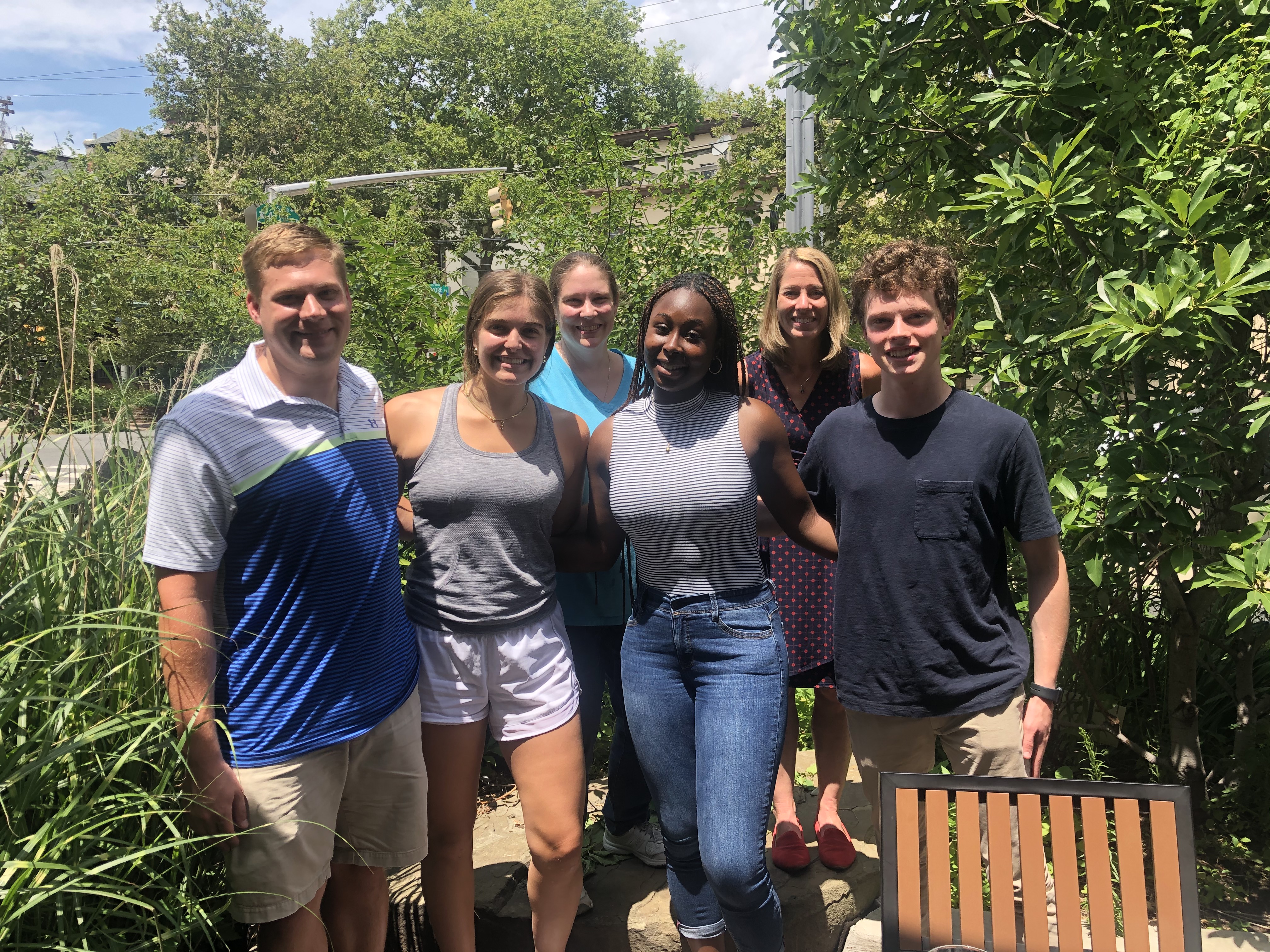 group of six people standing together outdoors in a garden