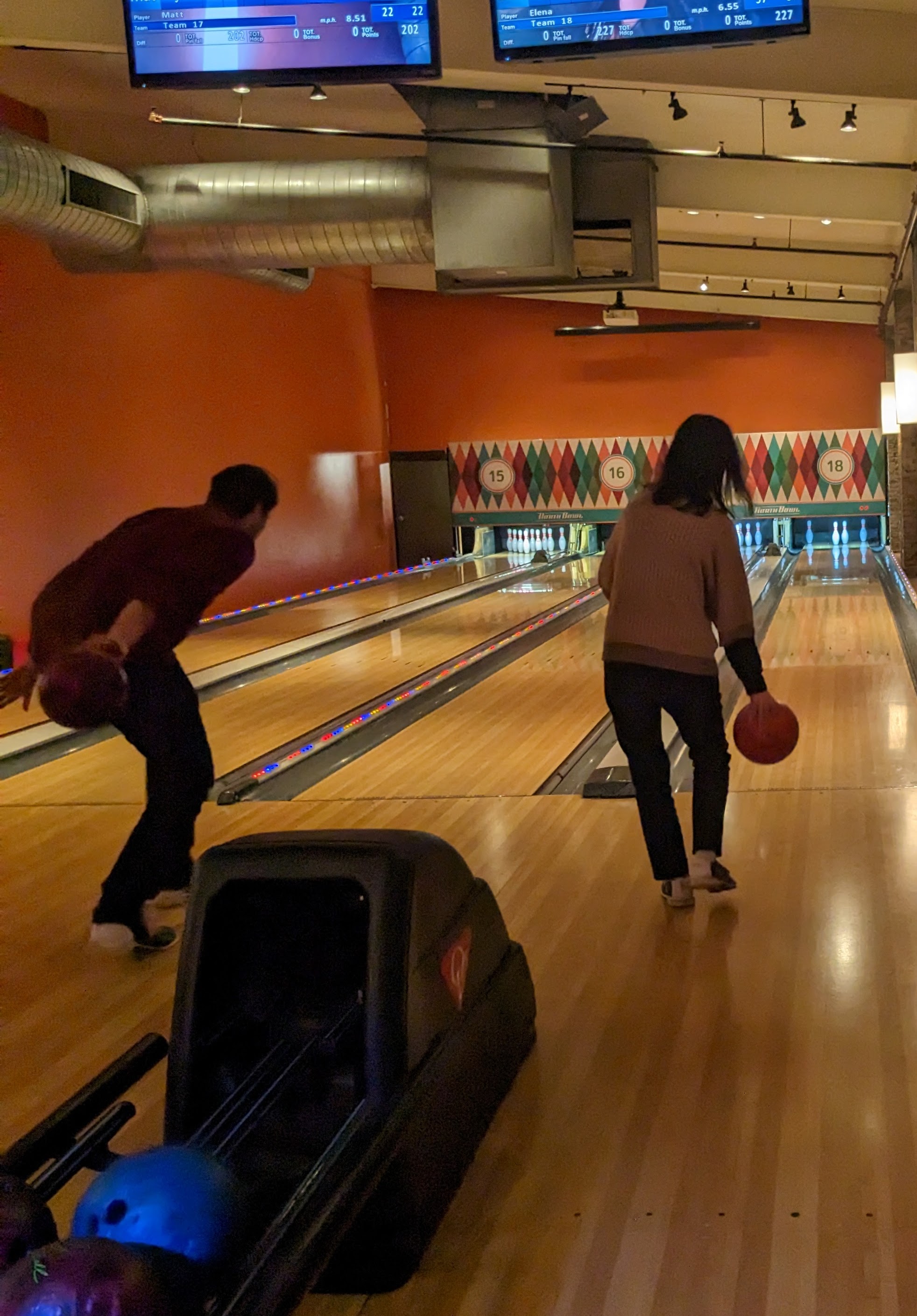 Picture of the backs of two lab members as they roll their balls down their lanes