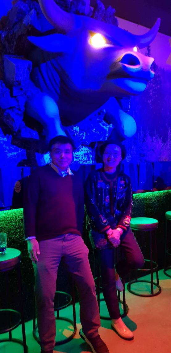 Two lab members sit on stools in front of a large bull head sculpture hanging on the wall