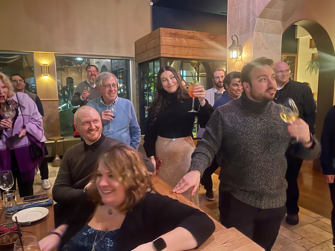 People standing and sitting at tables, some are holding drinks 